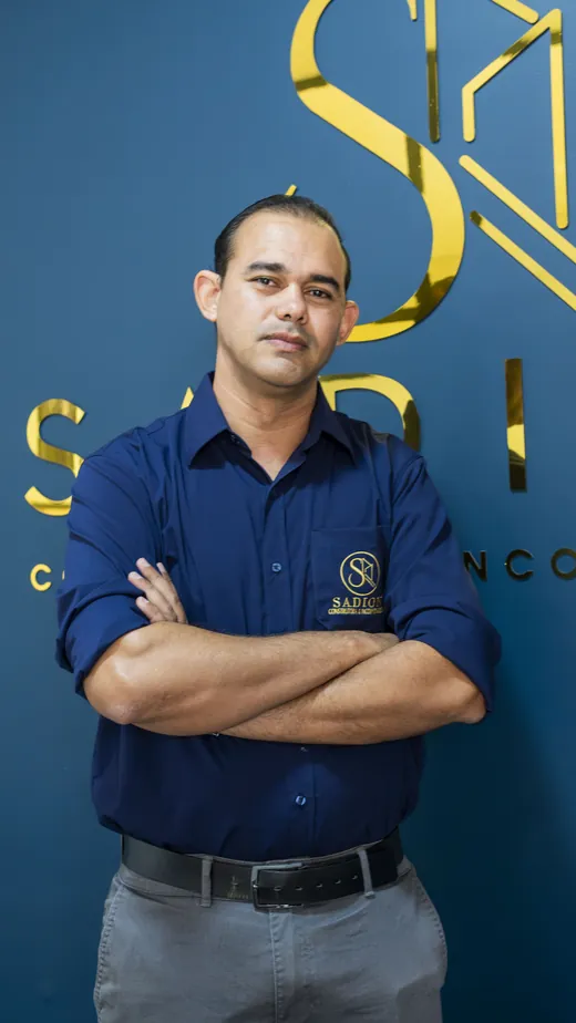 Integrante da equipe Sadion de braços cruzados em frente ao logotipo